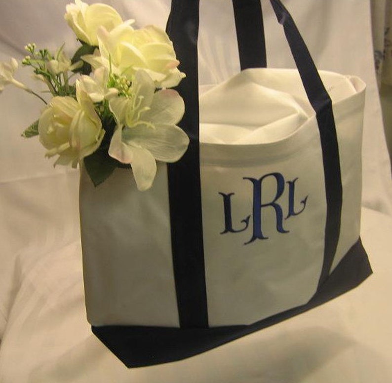 Puede incluir: Bolsa de lona blanca con asas negras e iniciales bordadas en azul "LRL". La bolsa est&aacute; decorada con un ramo de flores blancas.