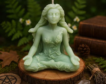 Könnte beinhalten: Eine hellgrüne Kerze in Form einer sitzenden Frau mit langem Haar und floralen Details. Die Kerze steht auf einer Holzscheibe, mit einem Hintergrund aus Grün, Büchern und einem Kristall.