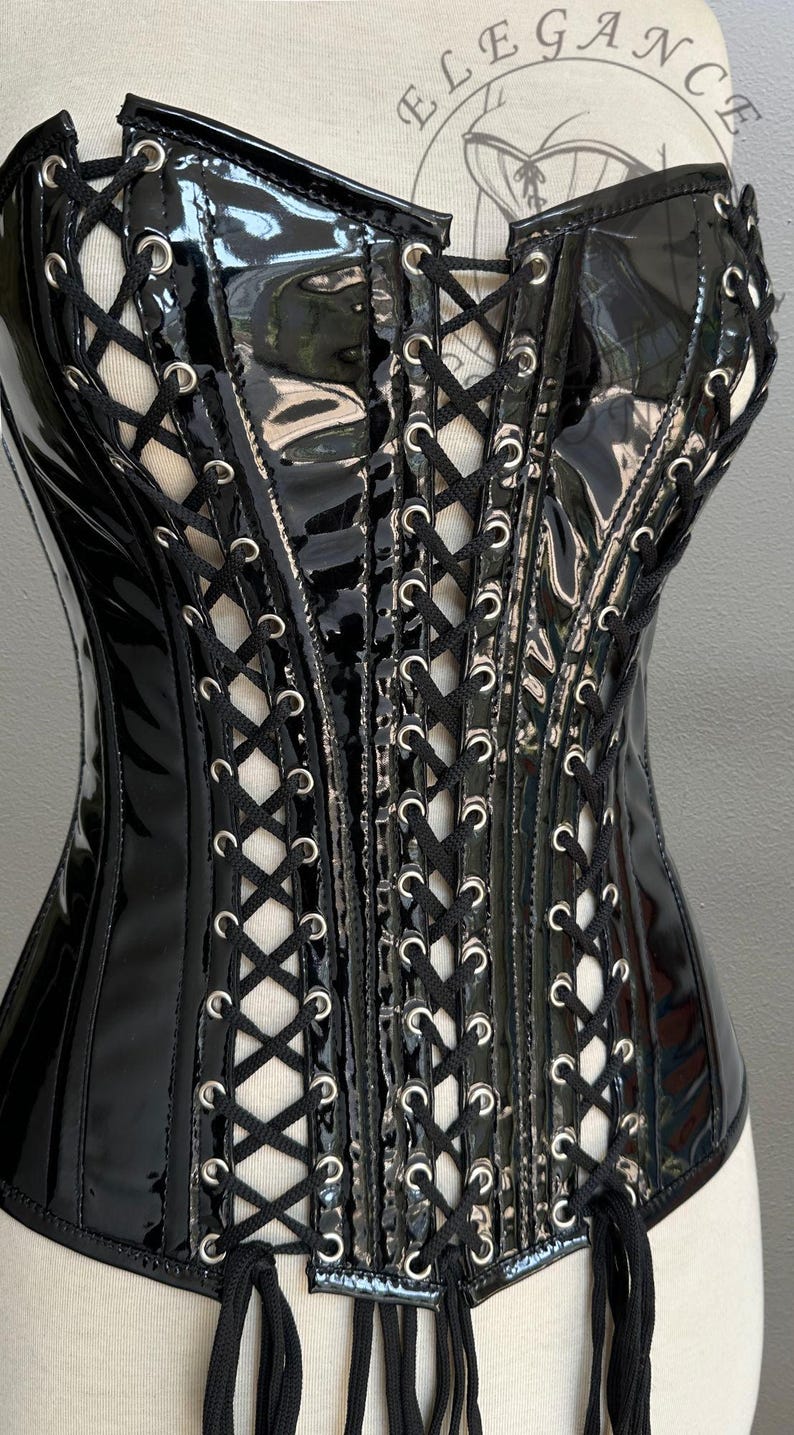 May include: Black patent leather corset with a lace-up front and silver-tone grommets. The corset features a structured design with a glossy finish and black lacing. A fashion item.