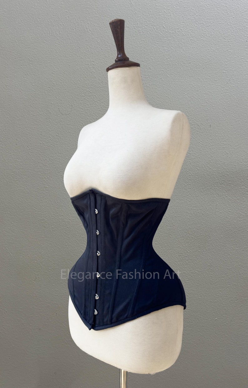 May include: A black corset with a satin finish and silver metal clasps. The corset is on a white mannequin. The text "Elegance Fashion Art" is visible on the corset.