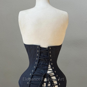 May include: Black corset with a lace-up back and metal eyelets. The corset is on a white mannequin. The text "Elegance Fashion Art" is visible on the corset.