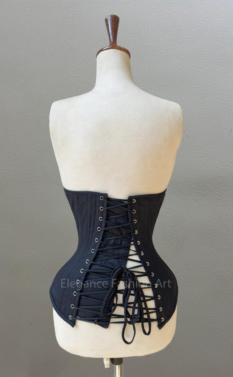 May include: Black corset with a lace-up back and metal eyelets. The corset is on a white mannequin. The text "Elegance Fashion Art" is visible on the corset.