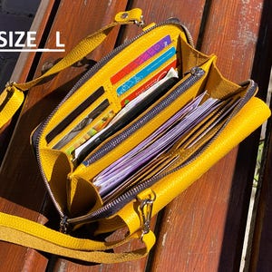 May include: A mustard yellow crossbody bag with a textured surface, featuring multiple interior compartments filled with various credit cards and paper currency. The bag includes a zipper closure and a matching yellow strap. The text SIZE L is visible.