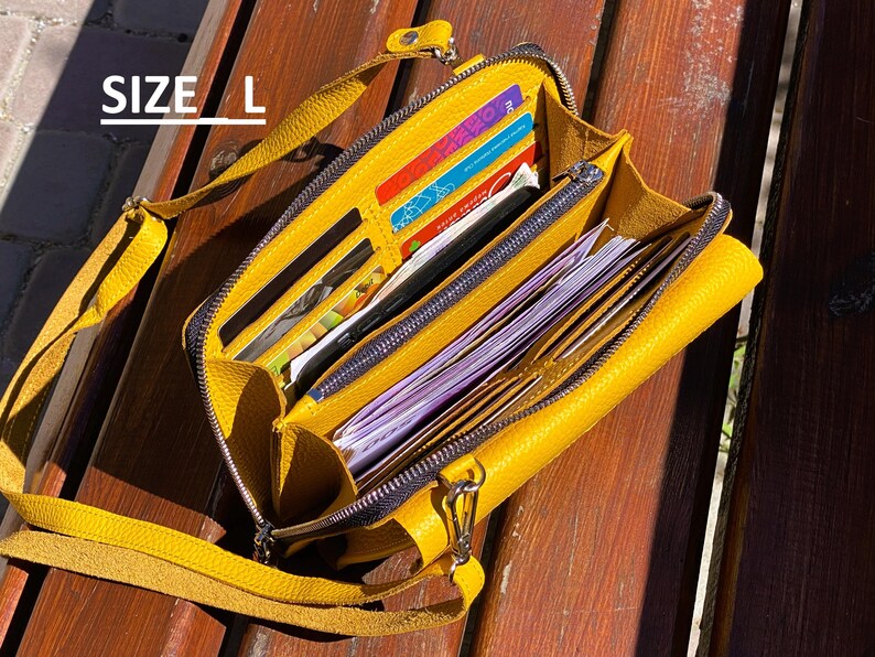 May include: A mustard yellow crossbody bag with a textured surface, featuring multiple interior compartments filled with various credit cards and paper currency. The bag includes a zipper closure and a matching yellow strap. The text SIZE L is visible.