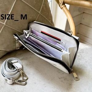 May include: A white textured leather crossbody bag with a black zipper closure and silver-toned hardware. The interior features multiple compartments containing paper currency and cards. The text SIZE_M is visible. A detachable white leather strap is included.