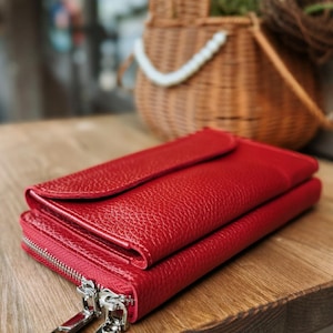 May include: A vibrant red wallet with a textured, pebbled surface. The wallet features a flap closure on the top section and a separate compartment secured by two silver-toned metal zippers with rectangular pulls, positioned on the side.