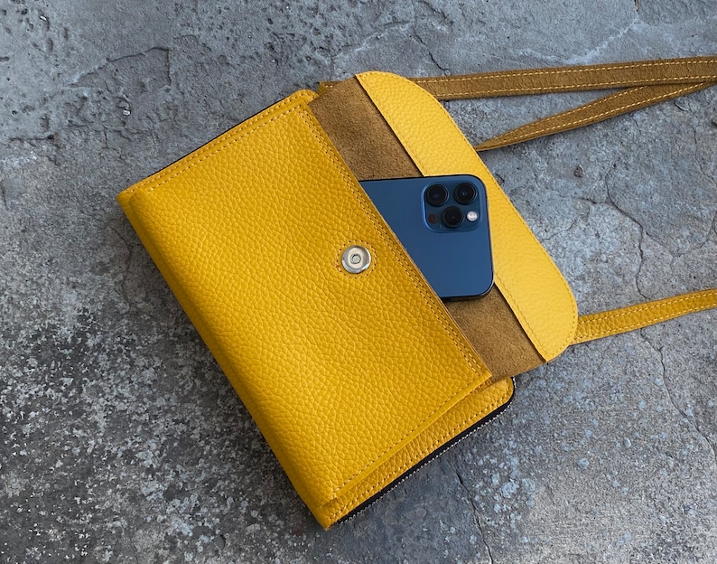 May include: A bright yellow textured leather crossbody bag with a flap closure secured by a silver-toned magnetic snap. The bag features a matching yellow shoulder strap and contains a dark blue smartphone tucked inside the open front pocket.