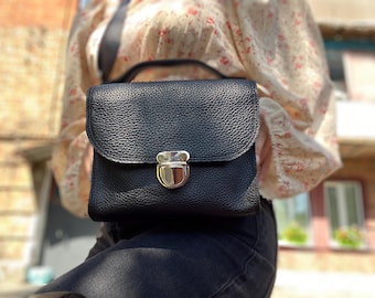 May include: A black leather satchel bag with a silver clasp. The bag has a textured surface and a small, rectangular shape.