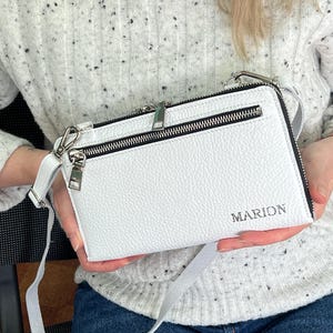 May include: A white rectangular crossbody bag with a pebbled texture, featuring a silver-toned zipper closure, a front zippered pocket, and a detachable shoulder strap. The name MARION is embossed in silver lettering on the lower right corner.