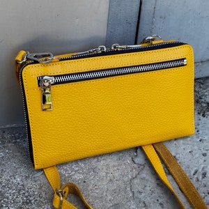 May include: A bright yellow rectangular crossbody bag with a textured surface. The bag features a horizontal silver-toned metal zipper pocket on the front, a black zipper lining, and silver-toned metal hardware including clips for a shoulder strap.