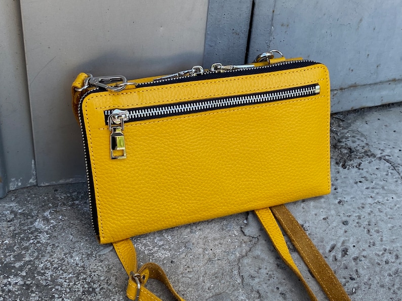 May include: A bright yellow rectangular crossbody bag with a textured surface. The bag features a horizontal silver-toned metal zipper pocket on the front, a black zipper lining, and silver-toned metal hardware including clips for a shoulder strap.