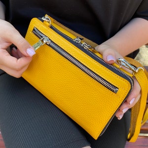 May include: A mustard yellow rectangular crossbody bag with a pebbled texture, featuring a prominent horizontal silver metal zipper on the front, a top zipper closure, and a matching yellow leather shoulder strap with silver metal swivel clips.