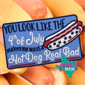 May include: A blue embroidered patch with the text "YOU LOOK LIKE THE 4th of July makes me want a Hot Dog Real Bad" and a hot dog graphic. The hot dog design features red, white, and blue colors with star accents. The patch is set against a background of hot dogs and buns.