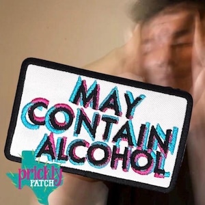May include: A rectangular embroidered patch with a white background and a black border. The text MAY CONTAIN ALCOHOL is stitched in black thread with a glitch-style effect featuring layered cyan and magenta outlines for a vibrant, retro aesthetic.