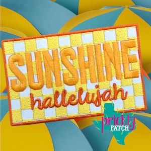 May include: Embroidered patch with the words "SUNSHINE" and "hallelujah" in orange script on a yellow and white checkered background. The patch has an orange border and a turquoise and pink logo in the bottom right corner.