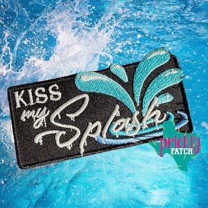 May include: Black rectangular patch with the words "KISS my Splash" embroidered in white script. A turquoise water splash design is above the text. The patch is set against a background of blue water with splashes.