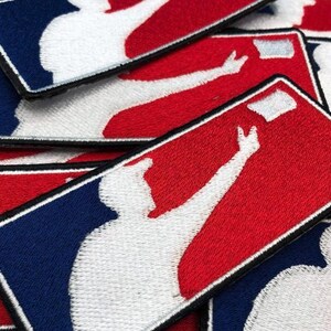 May include: A collection of rectangular embroidered patches featuring a white silhouette of a baseball player in a batting stance against a red and blue background. Each patch has a black stitched border and depicts a player reaching for a ball.