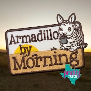 May include: Embroidered patch featuring the text "Armadillo by Morning" with a cartoon armadillo holding a mug. The patch has a rectangular shape with a brown border, a white background, and a yellow sun design.