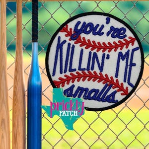 May include: A baseball-themed patch with the phrase "you're KILLIN' ME smalls" embroidered in blue on a white background, with red stitching details. The patch is round and has a black border. A blue baseball bat is visible, along with two wooden bats.