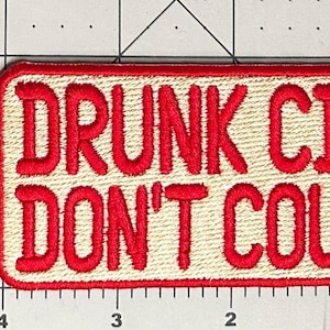 Pu&ograve; includere: Toppa ricamata con la scritta "DRUNK CIGS DON'T COUNT" in lettere rosse su sfondo beige. La toppa ha un bordo rosso e una forma rettangolare. La toppa &egrave; lunga circa 10 cm.
