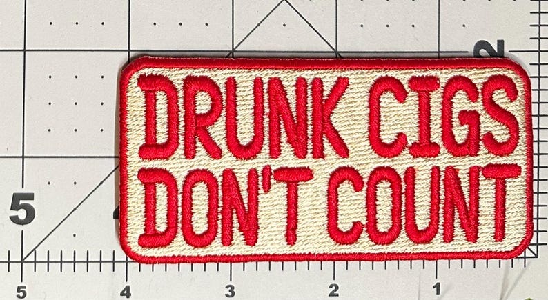 Pu&ograve; includere: Toppa ricamata con la scritta "DRUNK CIGS DON'T COUNT" in lettere rosse su sfondo beige. La toppa ha un bordo rosso e una forma rettangolare. La toppa &egrave; lunga circa 10 cm.