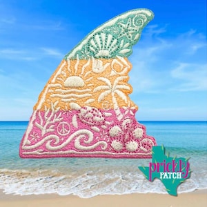 May include: An embroidered shark fin patch featuring a gradient design. The top section is teal with a starfish and shell, the middle is orange with a sun and palm tree, and the bottom is pink with a sea turtle, coral, and ocean waves.