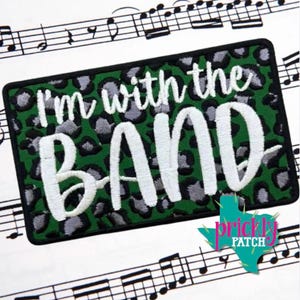 May include: A rectangular embroidered patch featuring a green and grey leopard print background with the white stitched text I'm with the BAND. The patch has a thick black border and is displayed against a background of musical staff lines.
