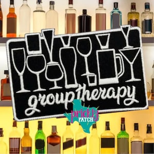 May include: A black sign with white outlines of various glasses and the words "group therapy." The sign is in front of a shelf with bottles of alcohol. The Prickly Patch logo is in the bottom right corner.