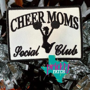 May include: A rectangular patch with the words "CHEER MOMS Social Club" in black script on a white background. A black silhouette of a cheerleader with pom-poms is in the center. The patch has a black border and the Prickly Patch logo.