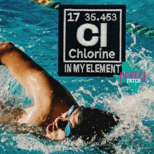 May include: A black and white embroidered patch with the text "Chlorine IN MY ELEMENT" and the chemical symbol "Cl". The patch is square and features the atomic number and weight. The background shows a swimmer in a pool.