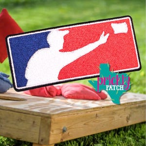 May include: A rectangular embroidered patch featuring a white silhouette of a person throwing a bean bag against a split blue and red background. The design mimics a sports logo with a black border. A teal graphic with the text Prickly Patch is visible.