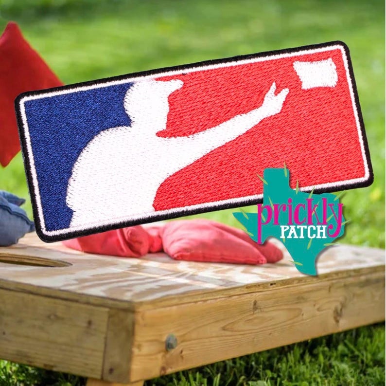 May include: A rectangular embroidered patch featuring a white silhouette of a person throwing a bean bag against a split blue and red background. The design mimics a sports logo with a black border. A teal graphic with the text Prickly Patch is visible.