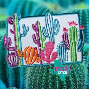 May include: Embroidered patch featuring a colorful cactus design. The patch showcases various cacti in shades of pink, green, orange, and blue, set against a white background. The patch is rectangular with a teal border. The text "Prickly Patch" is visible.