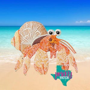 May include: Embroidered patch featuring a cartoon hermit crab with large, googly eyes. The crab is primarily orange and tan, with a detailed shell design. The background shows a beach scene with blue water and sky. The patch includes the text "prickly patch".