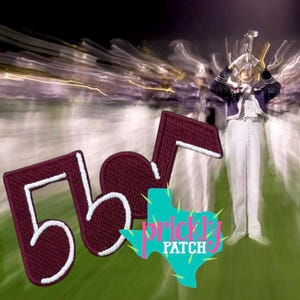May include: A maroon embroidered musical note patch with a white stitched border. The patch is layered over a blurred background image of a marching band member in a white and purple uniform playing a trumpet, with a teal Texas-shaped logo.
