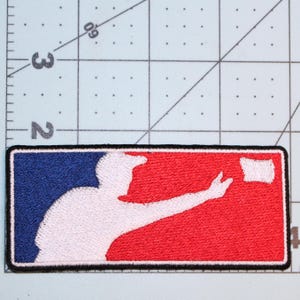 May include: A rectangular embroidered patch featuring a white silhouette of a baseball player on a split blue and red background with a black border. The patch is positioned against a cutting mat with visible inch markings, showing a width of 4 inches.