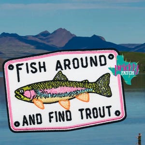 May include: Embroidered patch with a trout illustration and the text "Fish Around and Find Trout." The patch features a white background with a pink border, a colorful fish design, and black lettering. The background shows a lake and mountains.