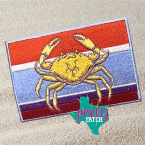 May include: Embroidered patch featuring a yellow crab on a rectangular background with red, white, blue, and purple stripes. The patch has a light blue border and the text "prickly PATCH" with a Texas outline.