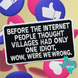 May include: A rectangular black embroidered patch with a white border and white text that reads: BEFORE THE INTERNET PEOPLE THOUGHT VILLAGES HAD ONLY ONE IDIOT, WOW, WERE WE WRONG. The patch is set against a background of blue and pink circular icons.