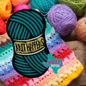 May include: A teal yarn ball patch with the text "KNIT HAPPENS" in yellow and white. The patch is surrounded by a black border. Colorful yarn balls and a crocheted blanket are in the background.