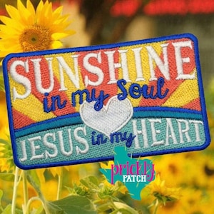 May include: Embroidered patch with the words "SUNSHINE in my Soul JESUS in my HEART" in white and blue lettering. The patch has a blue border and a heart in the center. The background is yellow, red, and blue.