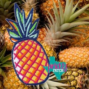 May include: Embroidered pineapple patch with a vibrant design. The pineapple features a blue and green crown, and a body with a pink, orange, and yellow diamond pattern. The patch has the text "Prickly Patch" in a turquoise Texas-shaped graphic.