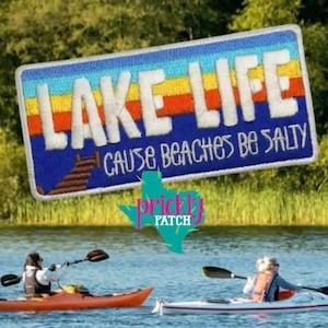 May include: Embroidered patch with the words "LAKE LIFE" in white block letters over a blue background with a colorful striped design. The text "CAUSE BEACHES BE SALTY" is below. The patch is displayed over a lake with kayakers.