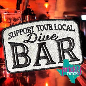 May include: Embroidered patch with the text "SUPPORT YOUR LOCAL Dive BAR" in black on a white background. The patch has a rectangular shape with rounded corners and a turquoise and pink cactus logo in the bottom right corner.