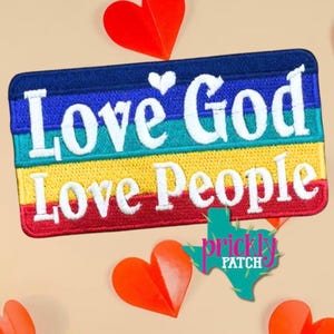 May include: A rectangular embroidered patch featuring horizontal stripes in blue, teal, yellow, and red. The white text reads Love God Love People with a small white heart above the word Love. The patch has a dark blue border and white stitching.