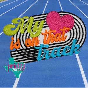 May include: Embroidered patch with the text "My heart is on that track" in green, orange, and blue. The patch features a pink heart and a black and white striped design, set against a blue background.