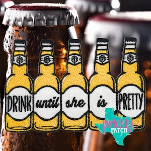 May include: An embroidered patch featuring five yellow beer bottles arranged in a row. Each bottle has a white label with one word of the black text "DRINK until she is PRETTY" printed across them. The patch has a black border and stitching.