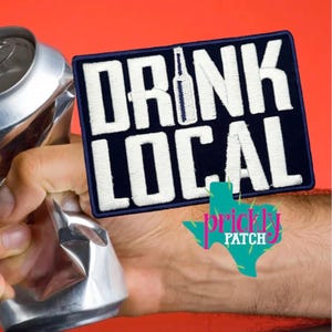 May include: A navy blue patch with white embroidered text that reads "DRINK LOCAL" with a bottle graphic. A crushed aluminum can is held in a hand. The Prickly Patch logo is in the bottom right corner.