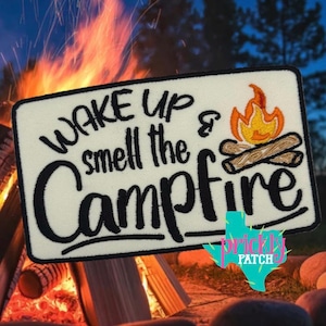 May include: A rectangular patch with the words "WAKE UP & smell the CAMPFIRE" in black script. A campfire graphic with orange and yellow flames and two logs is on the right. The patch has a white background and a black border. The Prickly Patch logo is at the bottom.