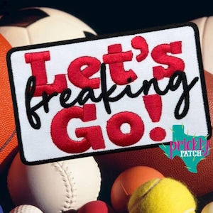May include: A rectangular embroidered patch with a white background and a black border. The text Let's is in red, freaking is in black cursive, and Go! is in red. The patch features bold, stitched lettering and is centered on a sports theme.